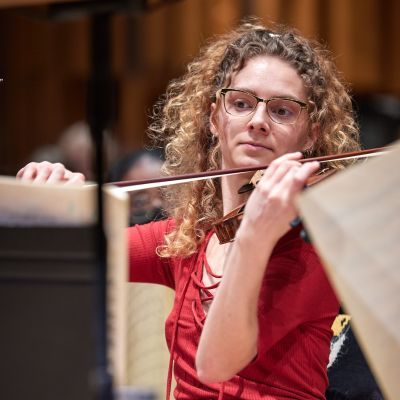 Violinist sitting straight with bow across the violin in a rehearsal